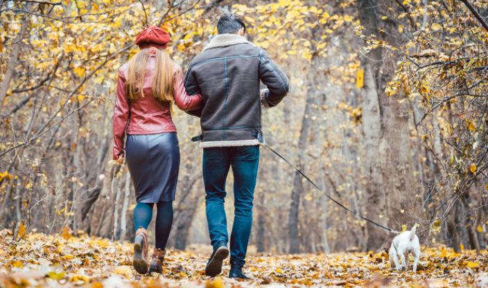 Paar geht durch Herbstlandschaft mit Hund spazieren