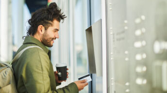 Mann steht mit Bankkarte vor Automat
