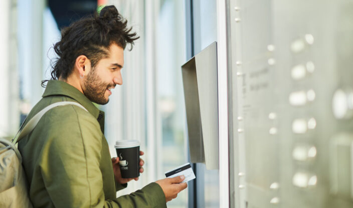 Mann steht mit Bankkarte vor Automat