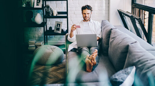 Mann sitzt auf Couch und kauft online ein