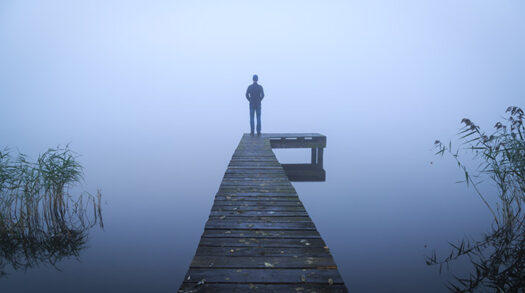 Person im Nebel am Ende eines Stegs