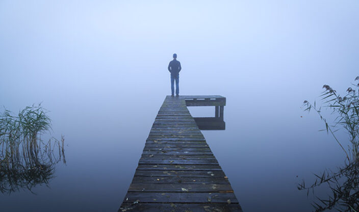 Person im Nebel am Ende eines Stegs